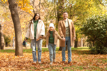 Fototapeta premium Happy parents with their little daughter holding hands in autumn park