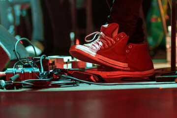 Closeup of a man’s feet pressing knobs on electric guitar pedals during a live performance, controlling sound effects and tone adjustments on stage