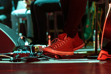 Closeup of a man’s feet pressing knobs on electric guitar pedals during a live performance, controlling sound effects and tone adjustments on stage