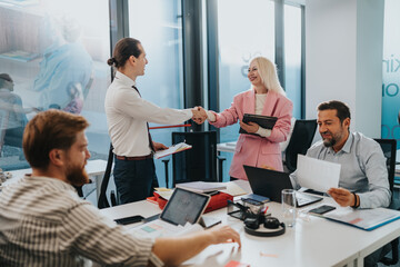 Colleagues celebrate agreement during a collaborative office discussion with laptops, documents,...