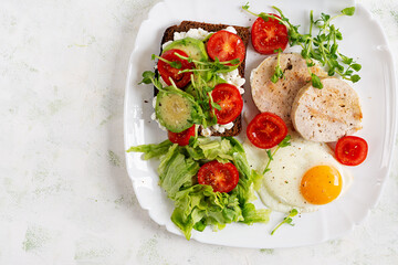 English breakfast. Fried egg, chicken meatloaf and sandwich with tomatoes, avocado and cheese. Top view