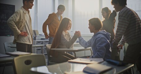 Cheerful Girl and Boy Arm Wrestle Playfully at Classroom Desk, Surrounded by Laughing Friends. Concept of Gender Equality, Emotional Openness, and Positive Communication Among Students. Static Shot.