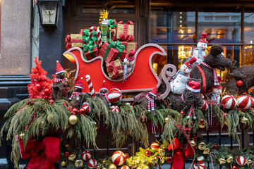 London, UK, Elaborate outdoor Christmas decoration featuring a red sleigh overflowing with presents, pulled by reindeer and snowmen figures, surrounded by festive greenery and ornaments.