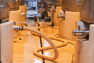 Naklejka premium Industrial plant floor showing a row of large processing tanks with stainless steel valves and connected hose, factory environment