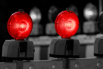 Red battery flash lights on a traffic barring indicating road closure, “no entry“ or “do not pass“ at construction site, accidents or blocked roads. Colorful lamps isolated on grayscale background.