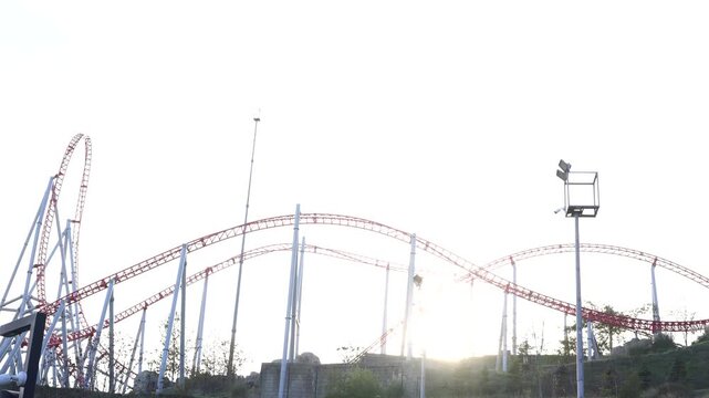 Red and white roller coaster track against bright sky