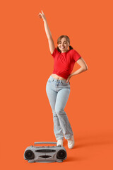 Young woman with boombox dancing on orange background