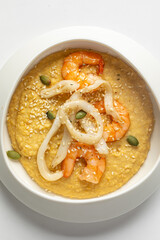 Creamy hummus topped with shrimp, squid rings, and capers served in modern white bowl on white background