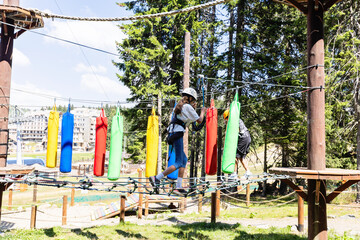 Young adventurer crossing elevated rope course in summer forest canopy challenge park