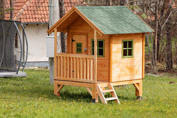 Small wooden playhouse with green roof, balcony and stairs in a backyard, perfect for kids to play in