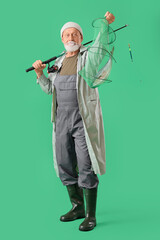 Senior man with fishing rod and caught fish in keepnet on green background