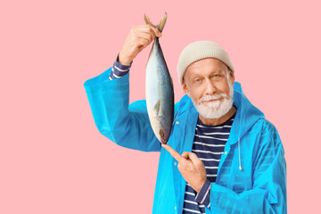 Senior fisherman with caught fish on pink background