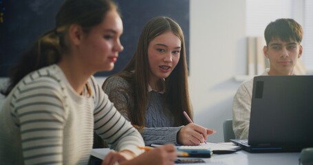 Close Up Two Female Students Working Side by Side at Shared Table. One Girl Writing Attentively in Notebook, Other, in Striped Sweater, Leans in, Looking at Papers. Concept Teamwork, Academic Support.