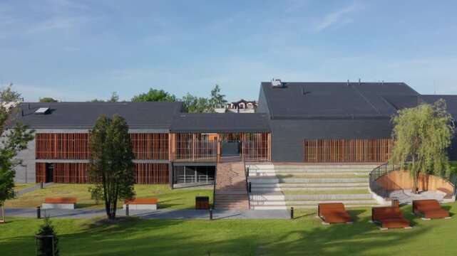 Aerial lateral movement along modern slate and timber-clad public pool, Eisenberga Street Krakow, with sun lounges in landscaped park setting.
