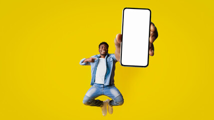 A joyful man jumps with excitement, holding up a smartphone in his hand against a vibrant yellow background. His upbeat expression suggests he is celebrating a special moment or event.
