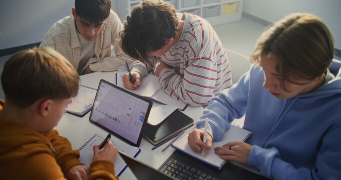 Small Group of Teenagers Engaged in Digital Learning Task, Centered Around Tablet Displaying Financial Charts or Graphs. Concept of Integration of Technology, Data Analysis and Visual Learning.