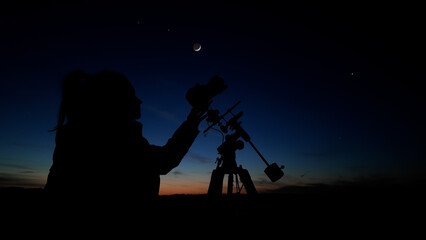 Amateur astro-photographer with a camera on a tripod photographing night sky with stars, planets, Moon and other celestial objects.
