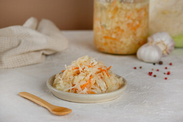 Fresh pickled cabbage, sauerkraut with carrot, garlic, and pepper on a table with wooden spoon.