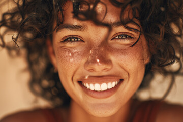 Radiant close-up portrait of a smiling young woman with curly hair and sun-kissed freckles, warm golden light, joyful expression and bright white teeth