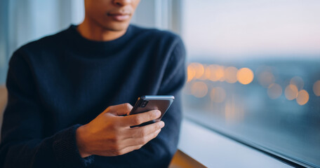 A person is using a smartphone while looking out of the window at night with city lights in the background