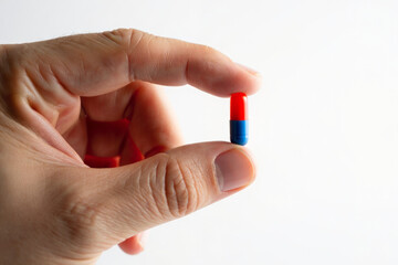 Close-up studio photo of hand holding small red and blue capsule on white background