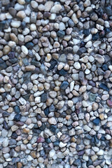 Close up texture of small, multi colored river pebbles embedded in concrete, often used for exposed aggregate wall finishes