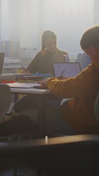 Students Collaborate on Laptops in Bright Classroom. Boy Sits Down at Table and Joins Teamwork. Group Project Work, and Essential Role of Digital Learning in Modern Educational Setting. Vertical Shot.