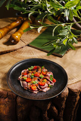 A beautifully arranged plate featuring sliced meat topped with fresh tomatoes sits on a rustic wooden table. Olive branches and a notebook add charm to the setting.