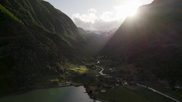 Aerial view of a valley with river cutting through green fields and dark mountains against a bright sky, Buarbreen Glacier, Odda, Vestland, Norway.