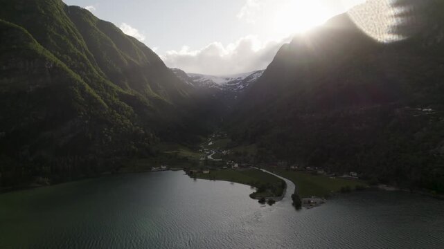 Aerial view of mountains surrounding the Buarbreen Glacier, contrasting the dark green of the forested slopes with the bright snow and sun, Odda, Vestland, Norway.