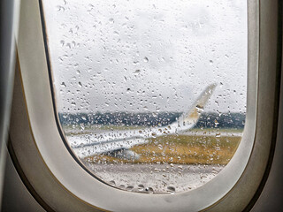Rain droplets on window as airplane prepares for takeoff at airport during cloudy weather