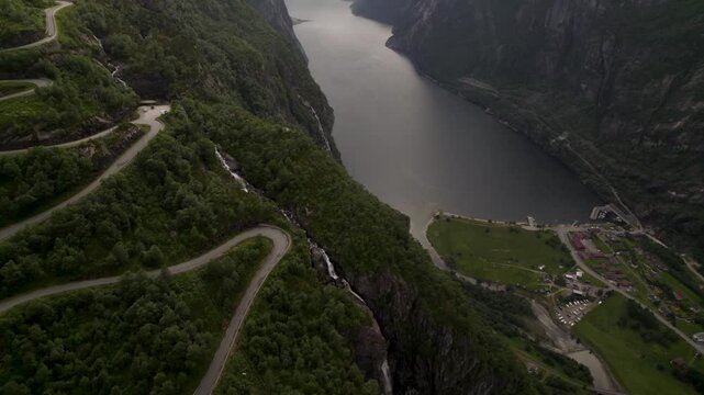 Aerial view of a winding road clinging to the green mountainside next to a deep fjord, a serene blend of nature and infrastructure, Lysebotn, Rogaland, Norway.