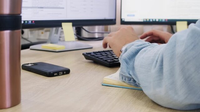 Person working at modern office desk with keyboard and dual monitors. Smartphone and coffee mug are on the desk. Digital workplace environment, productivity, everyday office work routine