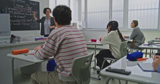 Focused Students Listen to Teacher Explaining Coding Assignment. Students Sit at Desks Attentively Following Teachers Explanation of Programming Concepts. Concept of Digital Education. Dolly Shot.