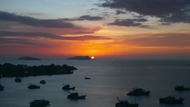 Stunning aerial view of the sunset behind Manukan Island from above the Kota Kinabalu waterfront harbor, with many trawler fishing boats silhouetted on the calm sea in Sabah, Malaysia.