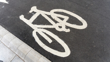 Obraz premium White bicycle symbol painted on asphalt beside curb marking city cycle lane