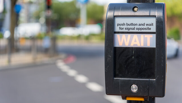 Pedestrian crossing wait button on black signal box beside city street intersection