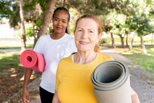 Senior women smiling after yoga class, carrying exercise mats in a park, enjoying friendship and active lifestyle