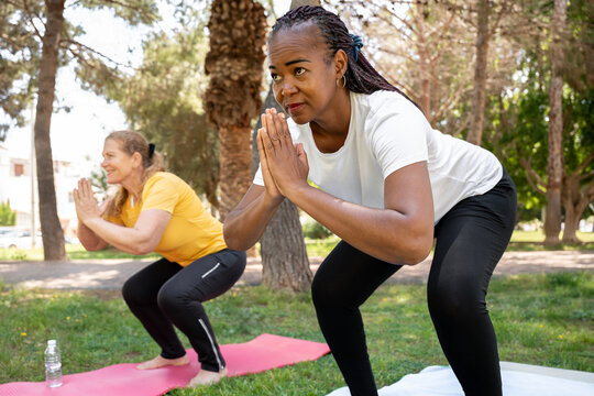 Two multiracial women engaging in yoga posture outdoors, enjoying a healthy lifestyle and active retirement - Powered by Adobe