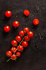 Ripe cherry tomatoes on the vine with coarse sea salt scattered on a dark textured surface. Organic food for cooking, healthy eating, and natural food concepts.