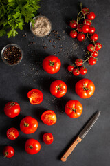 Fresh red tomatoes with parsley, sea salt, black pepper, and a kitchen knife on dark slate background. Cooking concept for organic food and healthy meals.