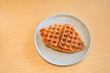 A crispy fish shaped waffle served on a light gray ceramic plate over a wooden table in natural light with a glass of single origin coffee. Perfect for restaurant, homemade bakery, or breakfast menu