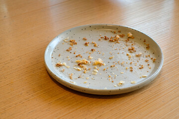 Top view of an empty gray ceramic plate with bread crumbs and food remains on a wooden table in natural light. Perfect for lifestyle blogs, restaurant ads, or food background designs