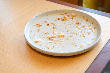 Top view of an empty gray ceramic plate with bread crumbs and food remains on a wooden table in natural light. Perfect for lifestyle blogs, restaurant ads, or food background designs