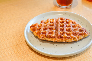 A crispy fish shaped waffle served on a light gray ceramic plate over a wooden table in natural light with a glass of single origin coffee. Perfect for restaurant, homemade bakery, or breakfast menu