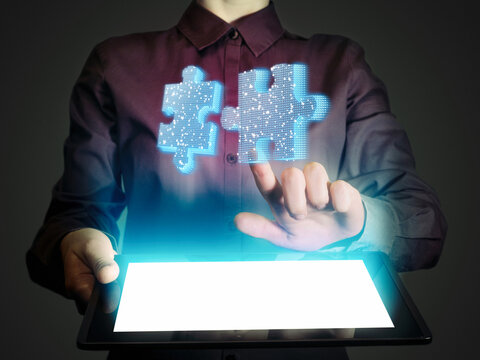 A business woman presses on a glowing holographic puzzle pieces. Concept of technology, innovation, digital connection, and teamwork on a dark blue background.