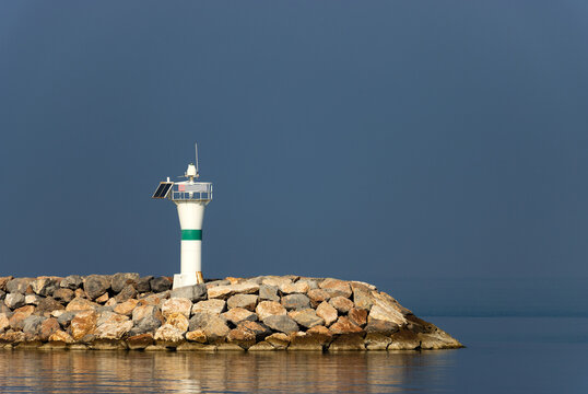 A green-striped breakwater lighthouse on a calm sea in very foggy weather. An important maritime structure in adverse weather conditions.