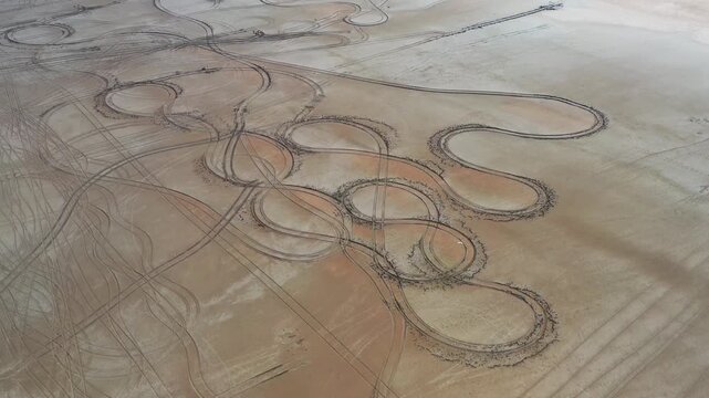 Aerial view of winding car tracks etched into the light brown, dry landscape of Tuz Lake, creating a stark contrast, Tuz, Ankara, Turkiye.