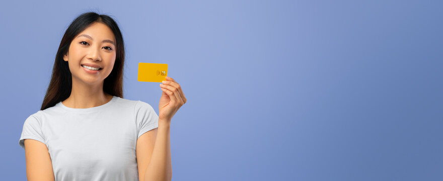 A woman stands with a bright smile, holding a yellow card in her right hand. Her casual outfit and cheerful demeanor create a positive atmosphere. The background is a calming light blue.