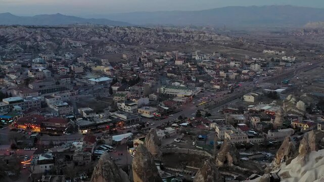 Aerial view of Goreme, a tapestry of houses nestled among fairy chimneys at dusk, contrasting with the rugged landscape, Goreme, Cappadocia, Turkiye.